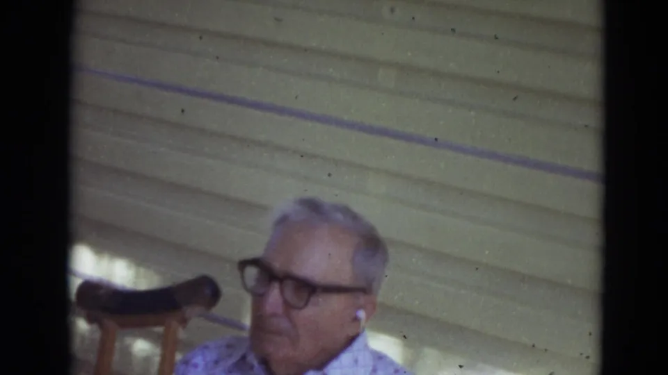 Older man in dark glasses and patterned shirt appears beside a porch chair in Lincoln, Nebraska home-movie footage.