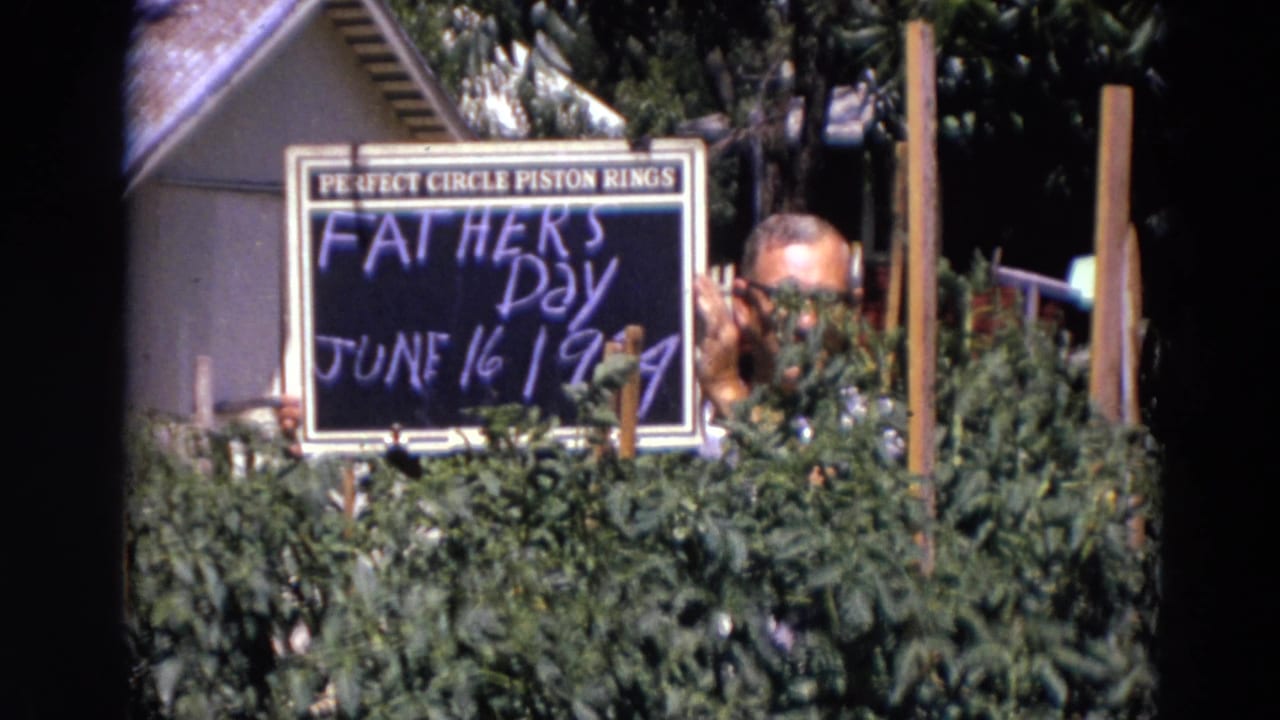 Man behind greenery holding a handwritten Father's Day sign.