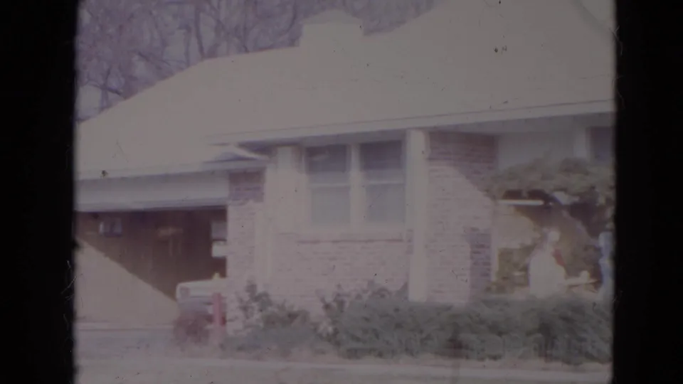 1974 Lincoln, Nebraska frame showing the camera panning left across a suburban house toward the garage and front shrubs.