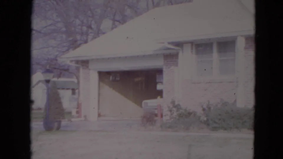 1974 Lincoln, Nebraska home-movie frame showing the garage and driveway side of a suburban brick-and-white house.