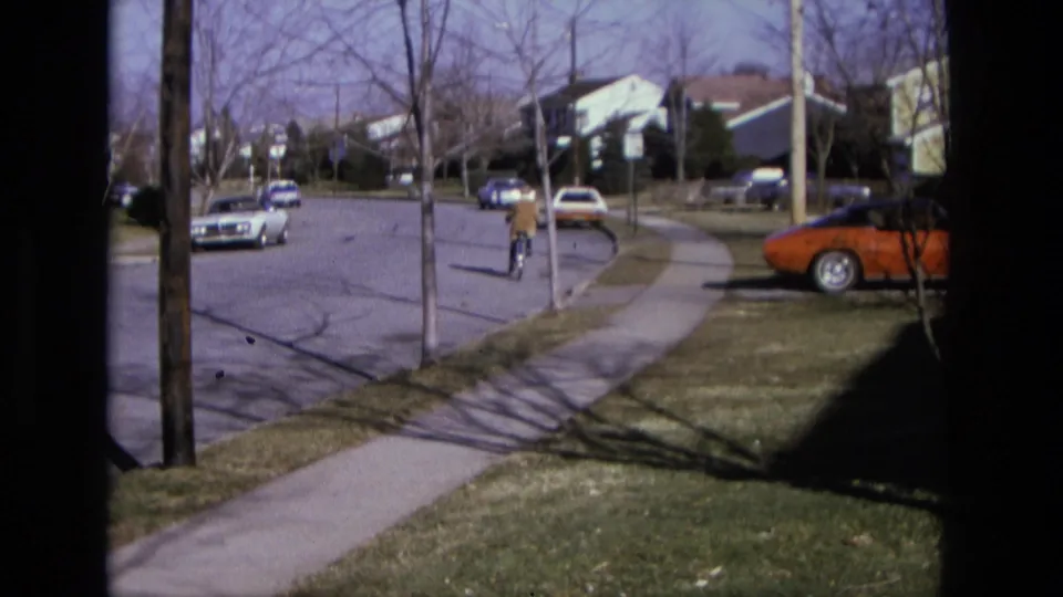 The final frame shows the bicyclist receding along a 1975 California suburban sidewalk, framed by parked cars and bare trees.