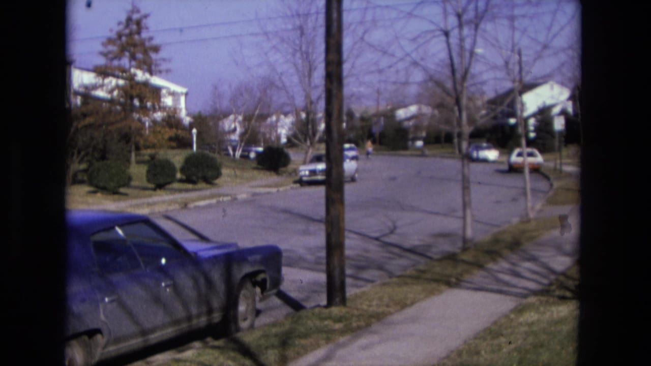 Suburban street with parked cars, houses, bare trees, and a distant bicyclist.