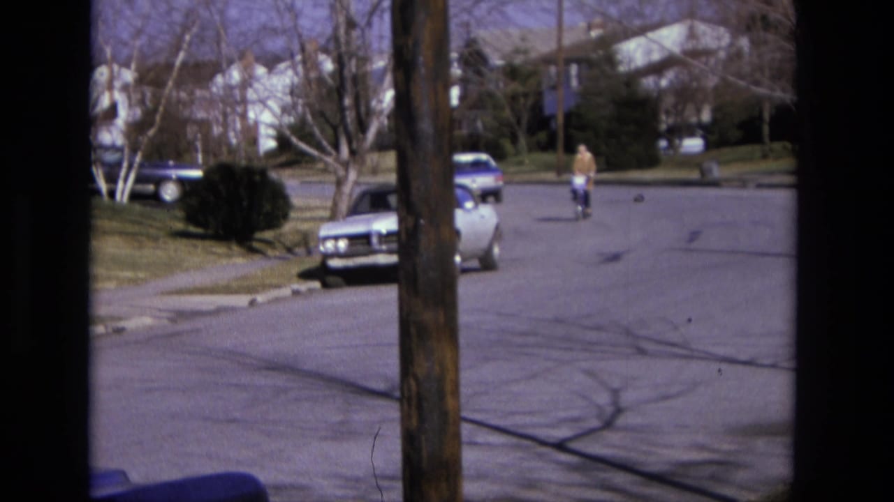 Cyclist continues along the street with parked cars, houses, and a utility pole in view.