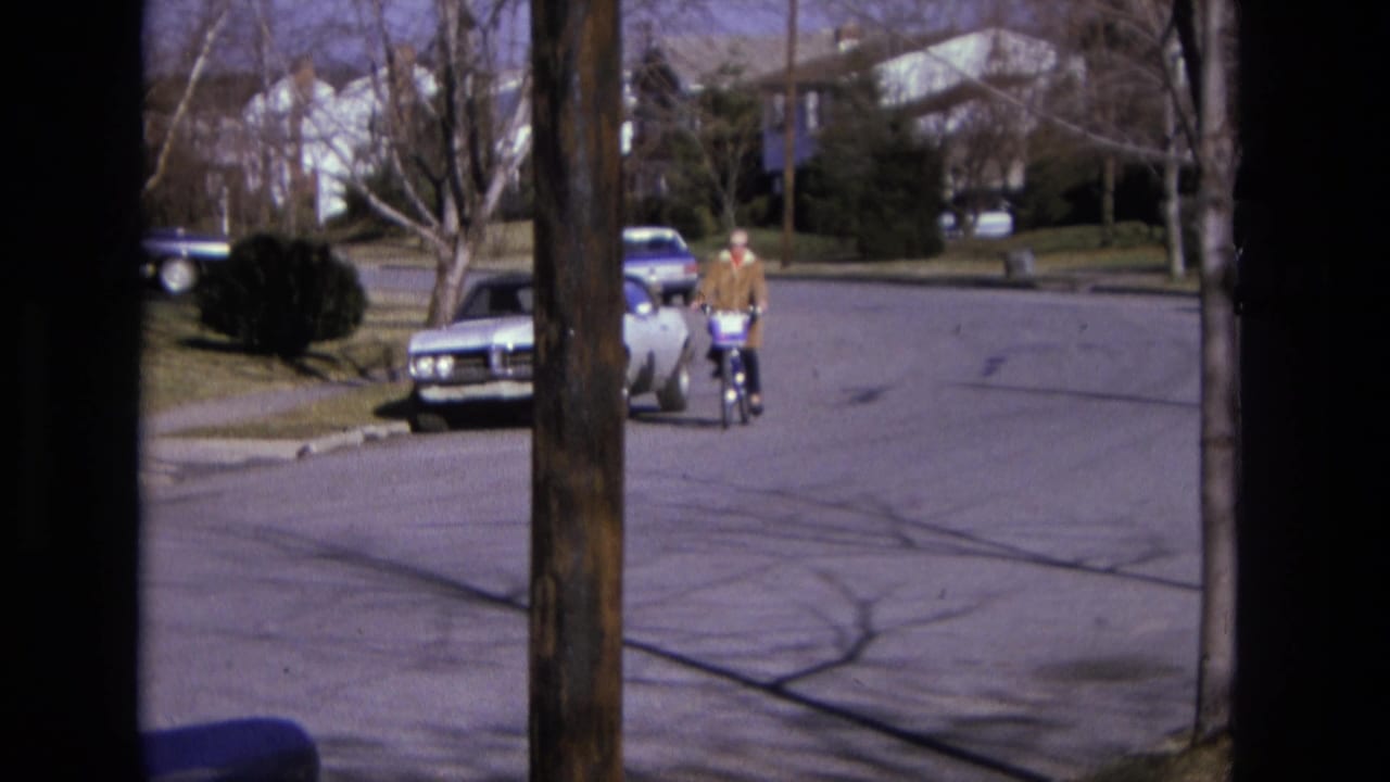 Cyclist riding on a suburban street past parked cars and leafless trees.