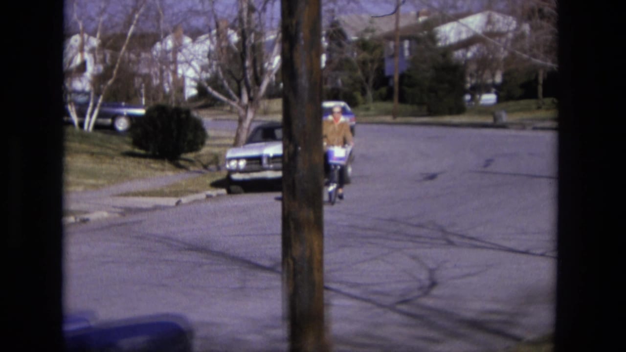 Cyclist continues along the street beside parked cars and a lawn.
