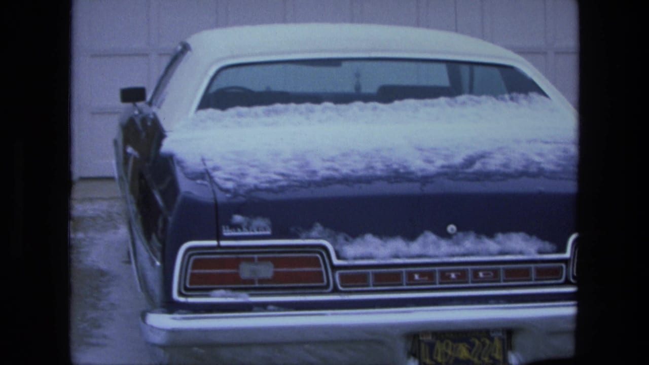 Rear three-quarter view of a snow-covered blue Ford LTD in front of a white garage door.