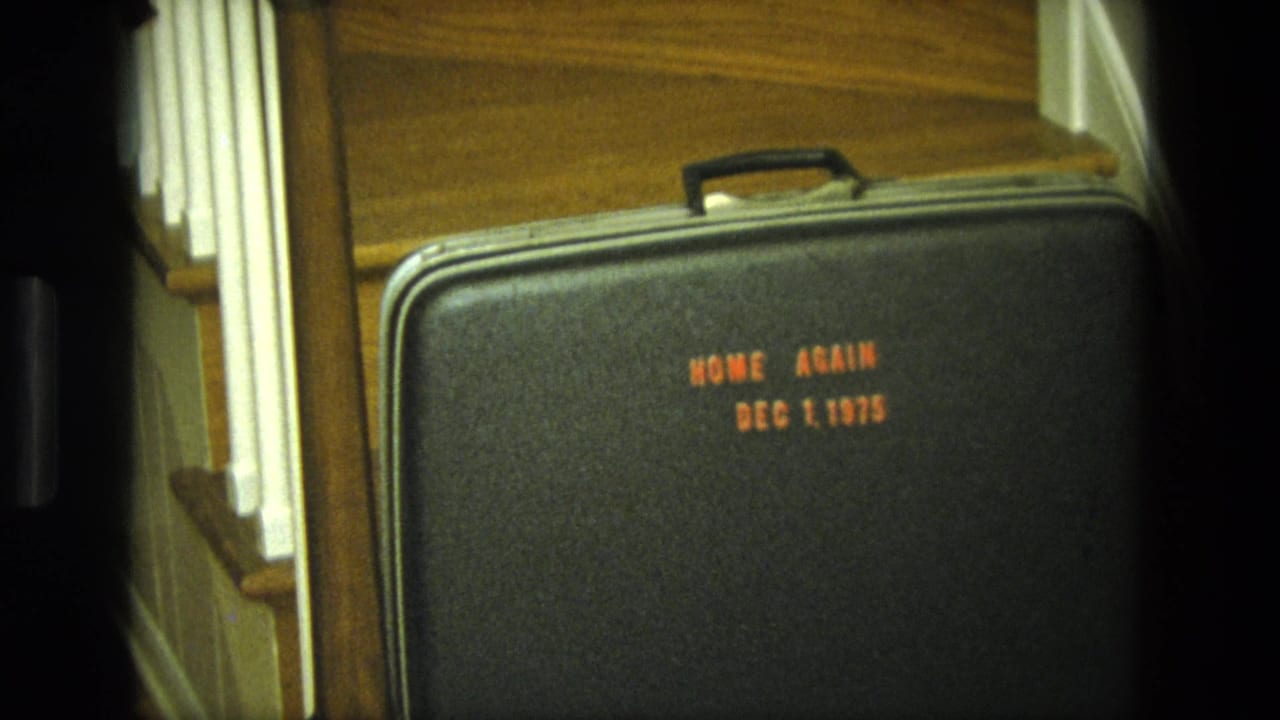 Black suitcase on wood stairs with orange text reading Home Again Dec 1, 1975.
