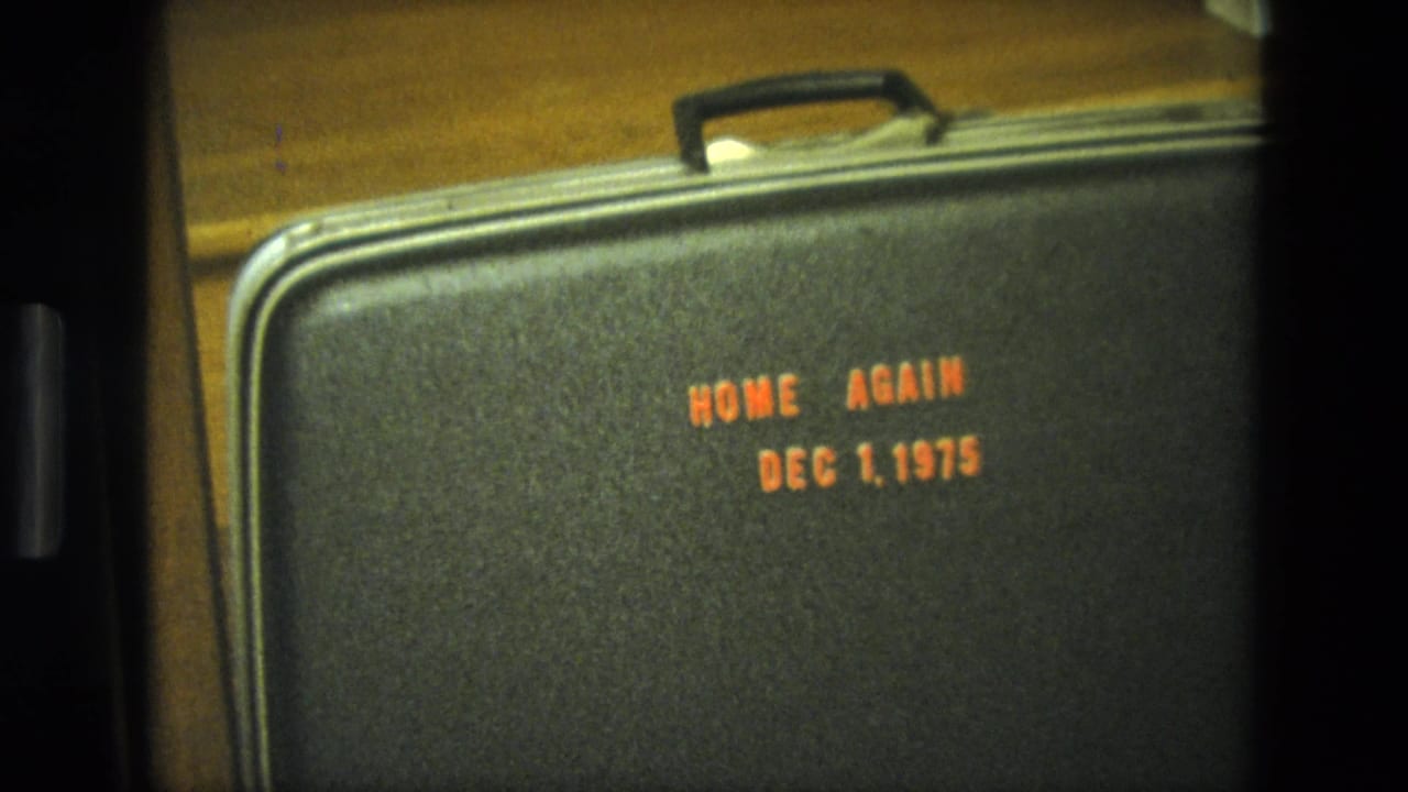 Close 1975 California home-movie view of a black suitcase marked Home Again Dec 1, 1975 on wooden stairs.
