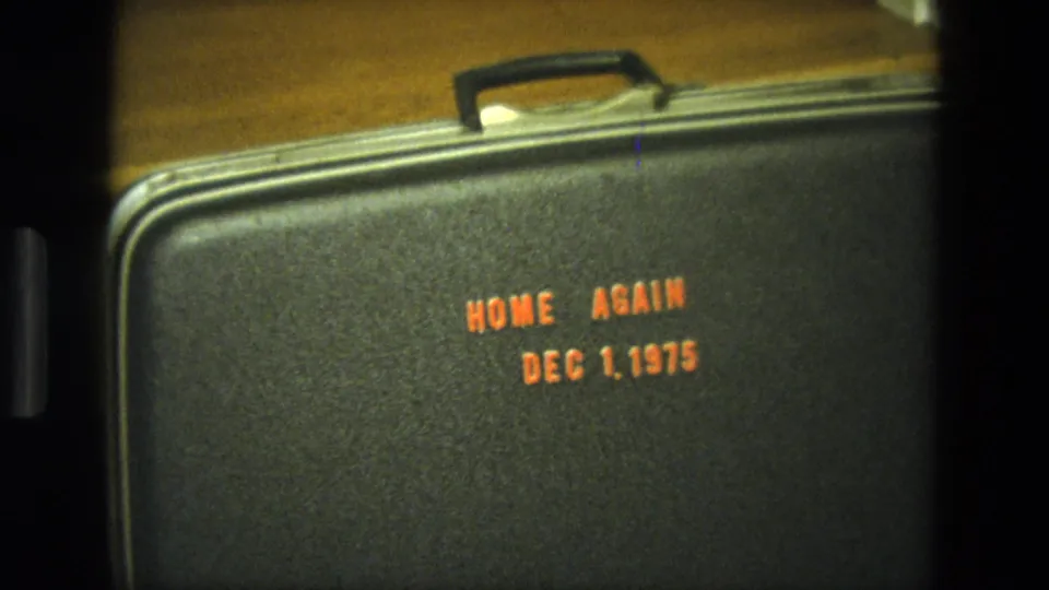 Final 1975 California home-movie frame of a black suitcase on wooden stairs, marked Home Again Dec 1, 1975.