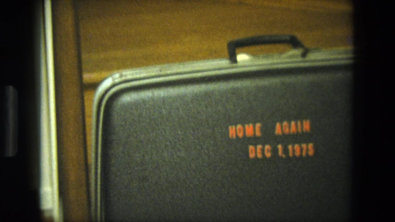 Black suitcase on wooden stairs with orange text reading HOME AGAIN DEC 1, 1975.