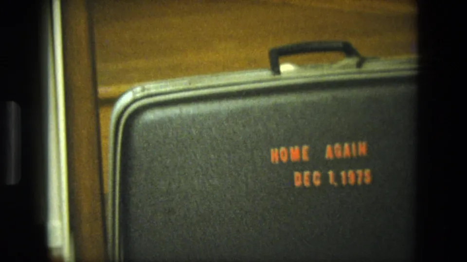 1975 California 8mm frame showing a black textured suitcase on wooden stairs with orange homecoming date text.