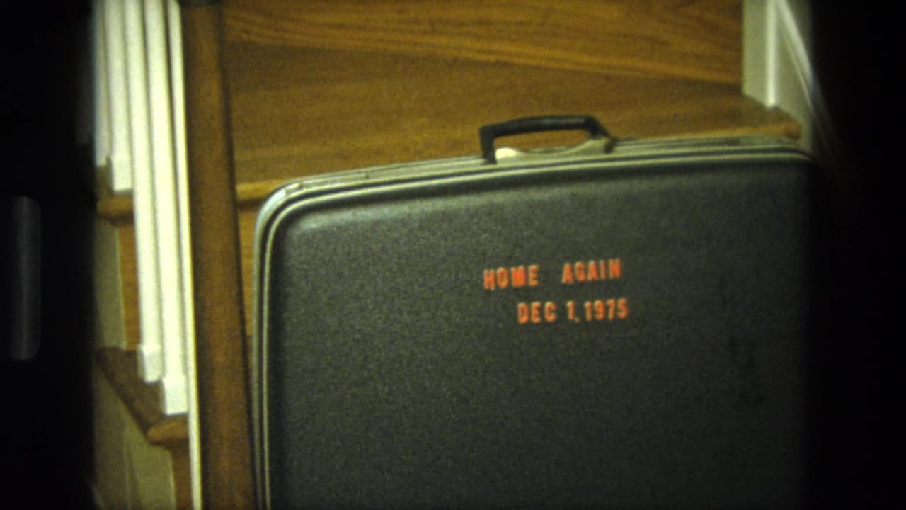 Black suitcase on stairs, framed wider with orange HOME AGAIN and date text visible.
