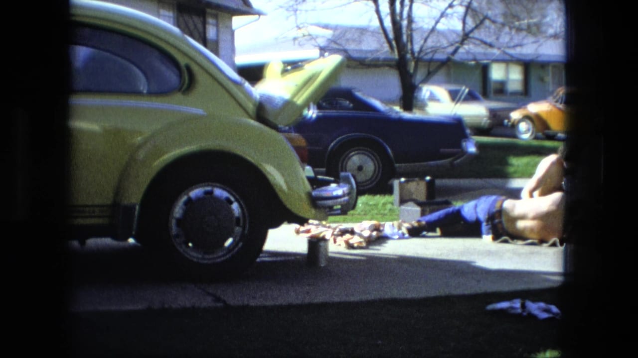 Yellow Beetle at left with open hood, tools on the driveway, and a person partly visible at right.
