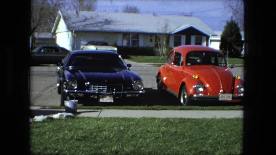 The closing frame shows parked cars, including a red Beetle and dark sedan, outside a Fort Wayne suburban house in 1976.