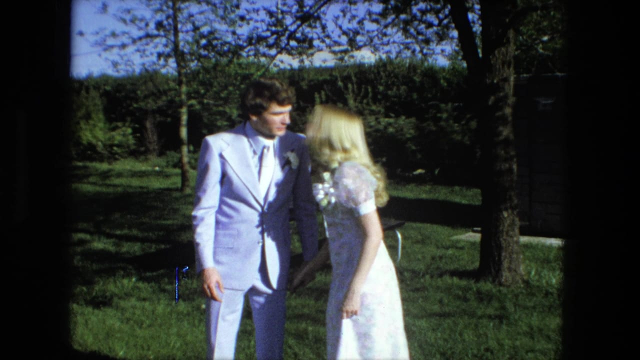 Bride and groom stand close together on a sunny lawn beside trees.