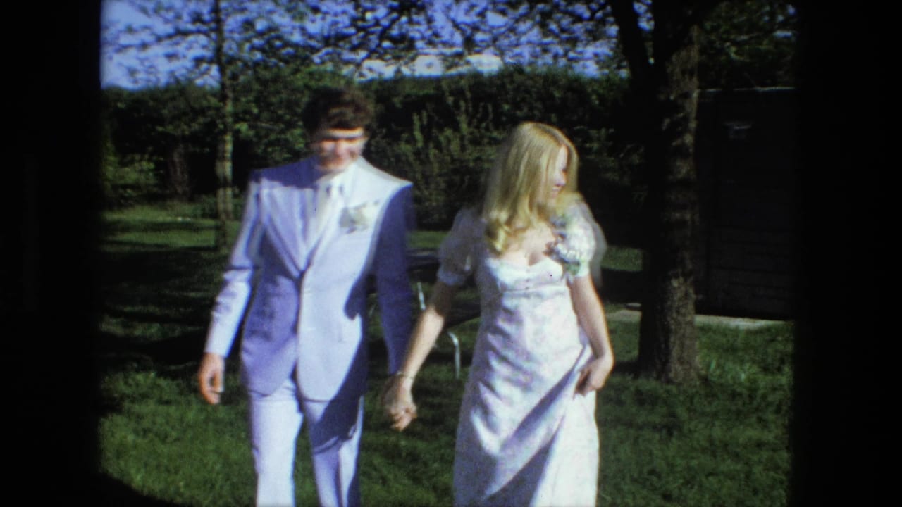 Bride and groom hold hands while walking across a grassy yard.