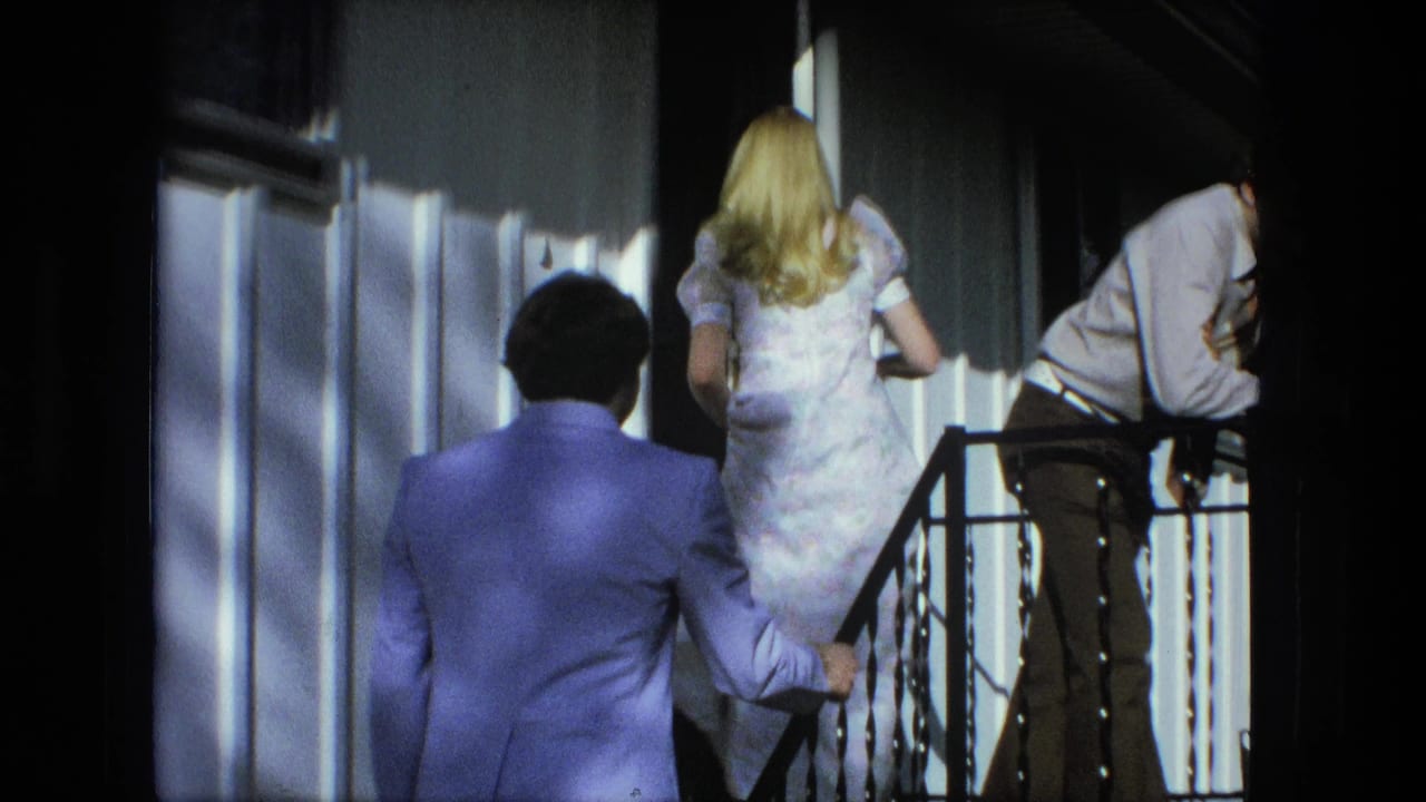 The couple continues up the porch steps in Fort Wayne, with a second young man leaning near the railing in the sunlit frame.