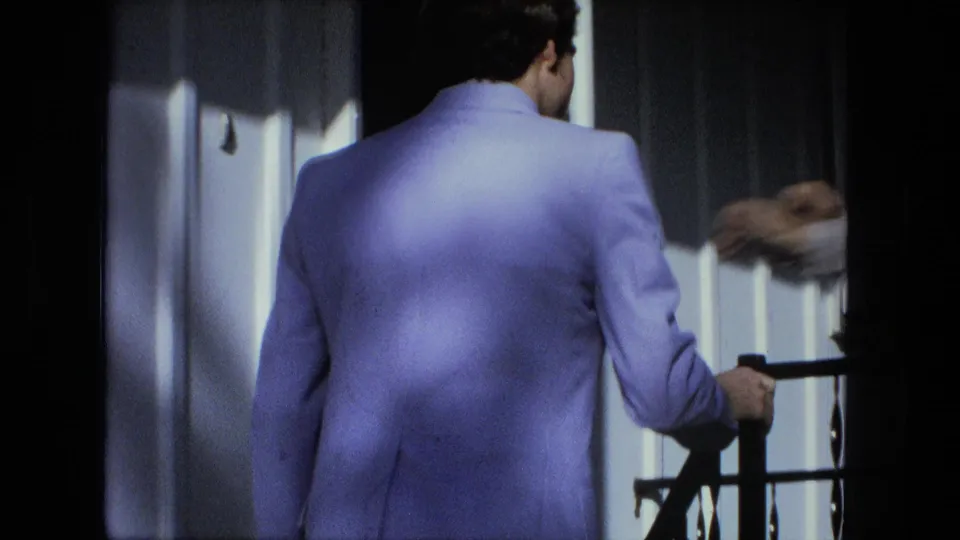 A Fort Wayne 1976 home-movie frame shows the man from behind on the porch stairs near the door and railing.
