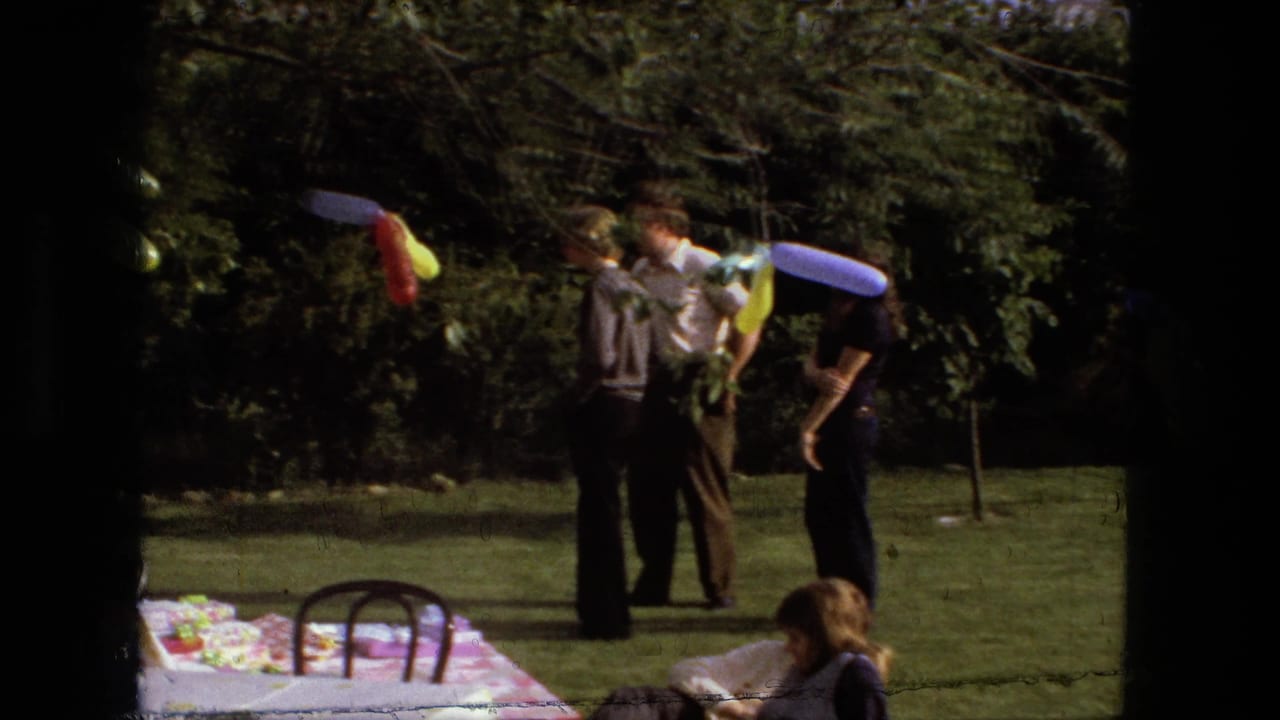 Adults standing on a lawn near colorful balloon decorations and a picnic table.