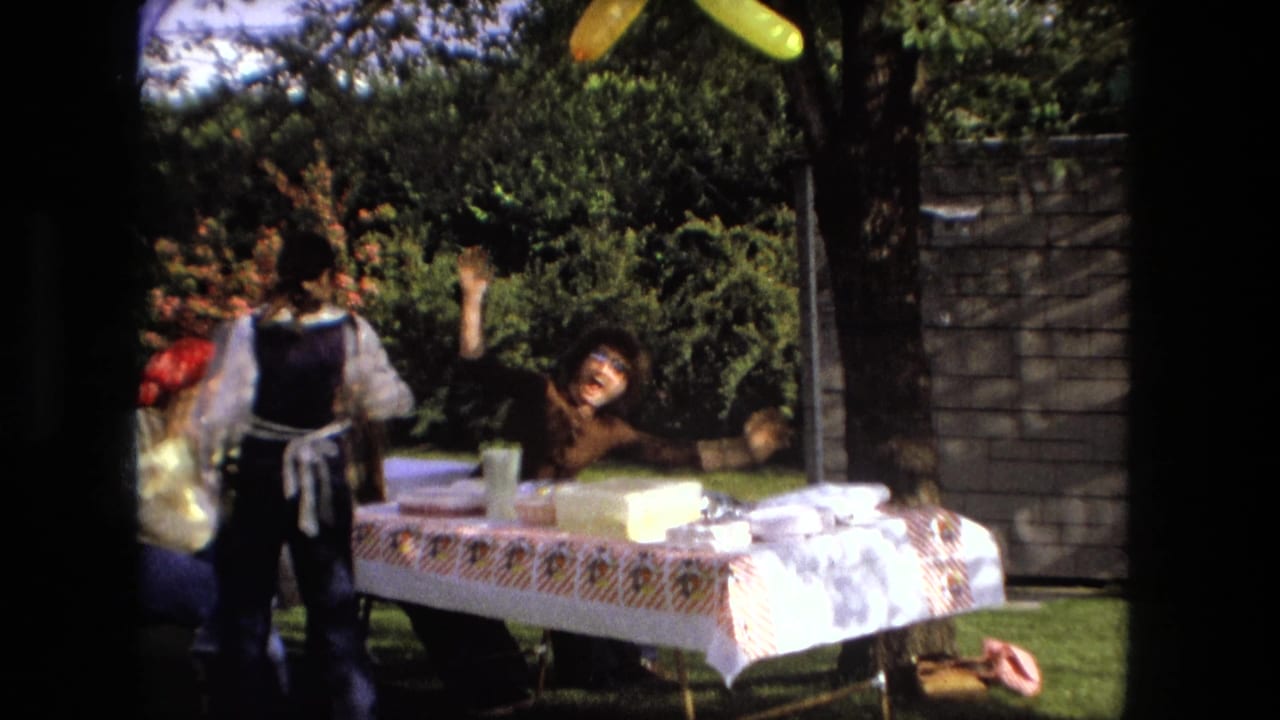 Young man leans backward beside a picnic table in a sunny backyard.