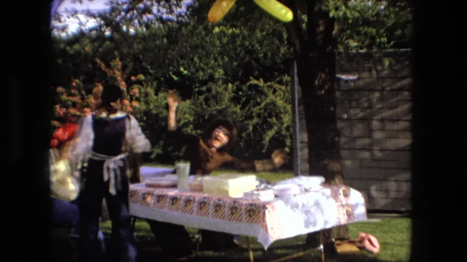 In Fort Wayne, Indiana, 1976, a young man performs a comic fall near a picnic table during a backyard gathering.