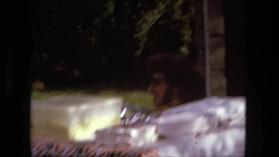 A soft 8mm frame shows the checked picnic table and containers while the young man is partly obscured behind the table.