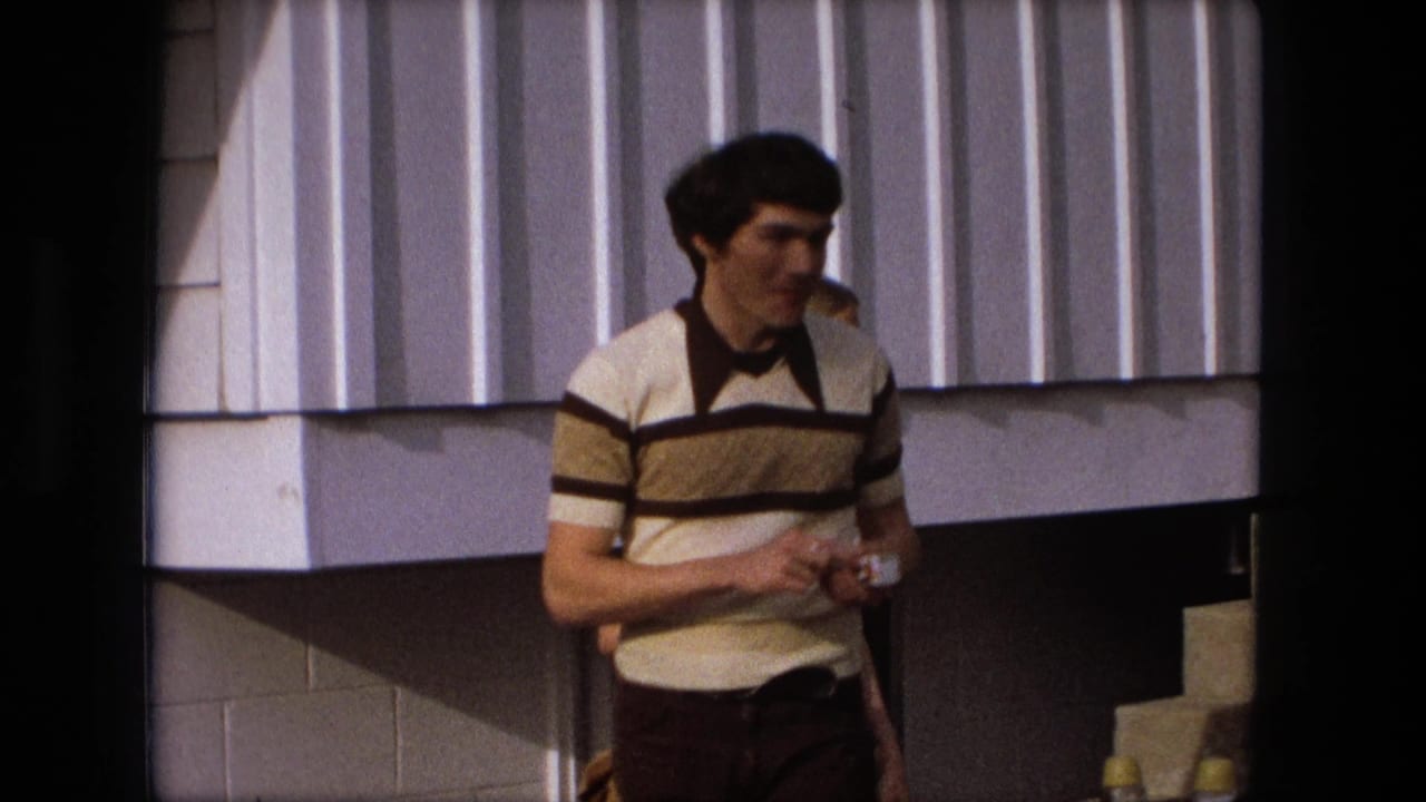 Young man in a striped shirt stands near a building exterior holding a small cup.
