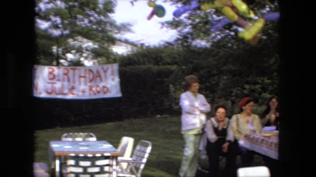 Backyard birthday banner hangs near picnic tables as guests gather on a lawn.
