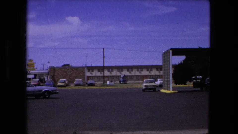 1976 Fort Wayne roadside motel lot with parked cars, partial convertible at left, and covered entry architecture at right.