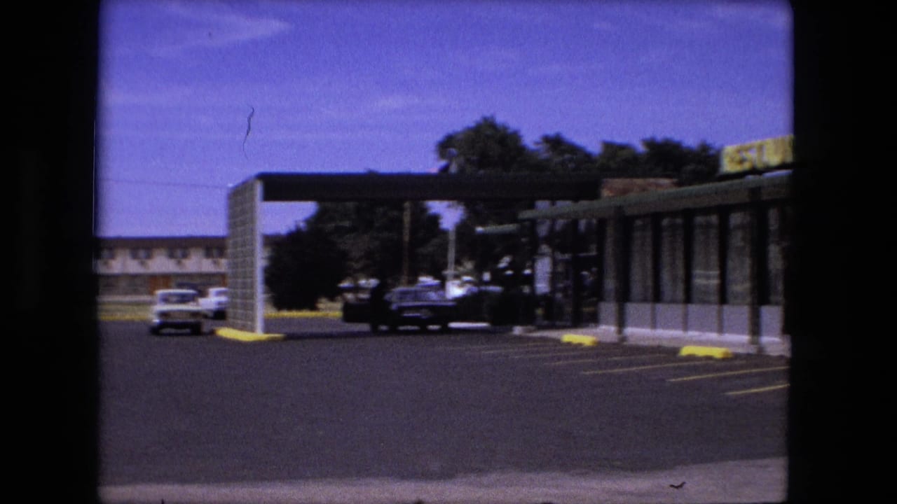 1976 Fort Wayne roadside restaurant exterior with a yellow sign, brick wall, covered walkway, yellow curb stops, and a few cars in a mostly empty parking lot.