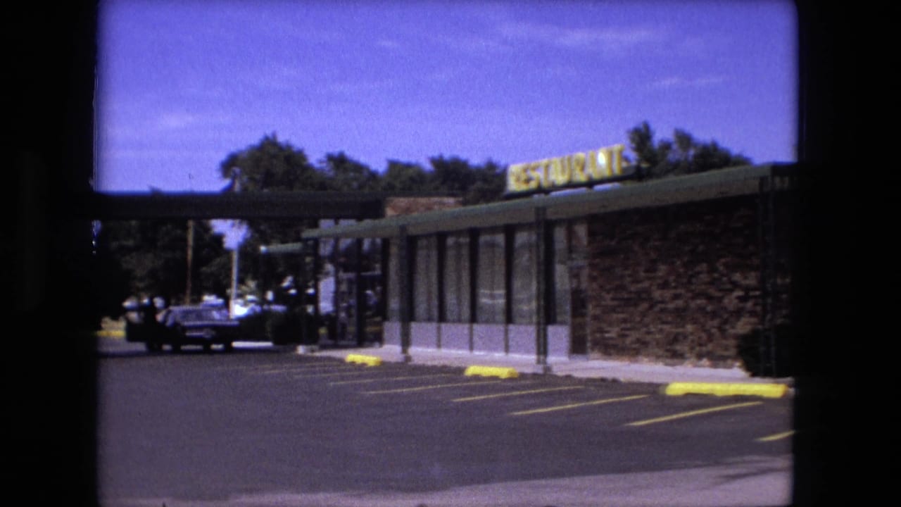 Fort Wayne restaurant frontage in 1976, showing a readable yellow sign, brick exterior, large windows, yellow parking curbs, and cars near the walkway.