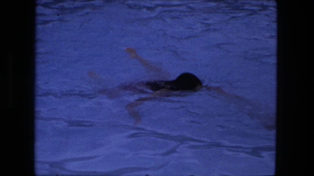 Swimmer moving through blue-tinted pool water with one arm raised.