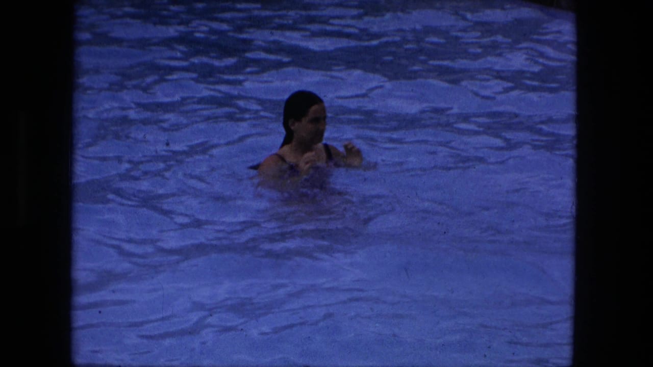 A young woman appears to tread water in a blue-tinted swimming pool, seen in archival 8mm footage from the Fort Wayne metadata context.