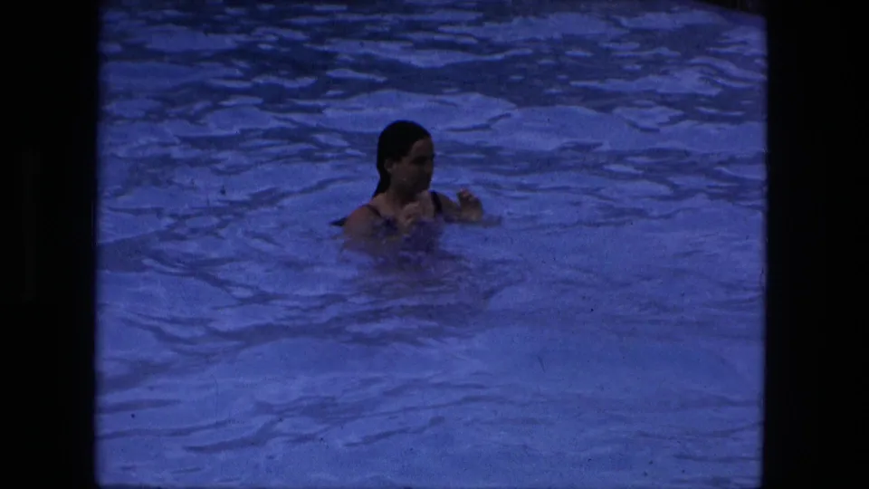 A young woman appears to tread water in a blue-tinted swimming pool, seen in archival 8mm footage from the Fort Wayne metadata context.