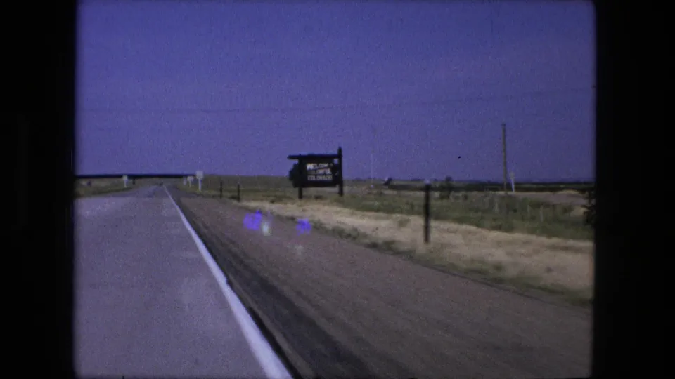 8mm frame near Fort Wayne, Indiana, showing a rural highway approach to a bridge, with a signpost and utility poles along the right side.