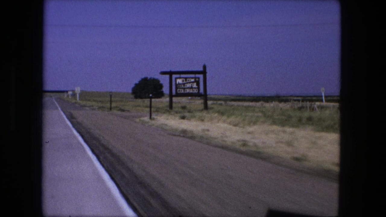 Wooden sign reading Welcome to Colorful Colorado beside a rural road and open fields.