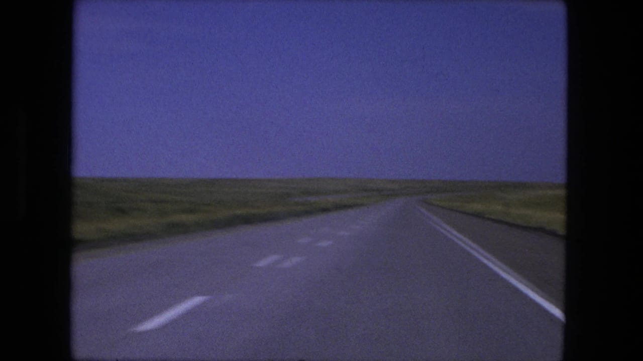 Straight highway receding through open grassland under a blue sky.