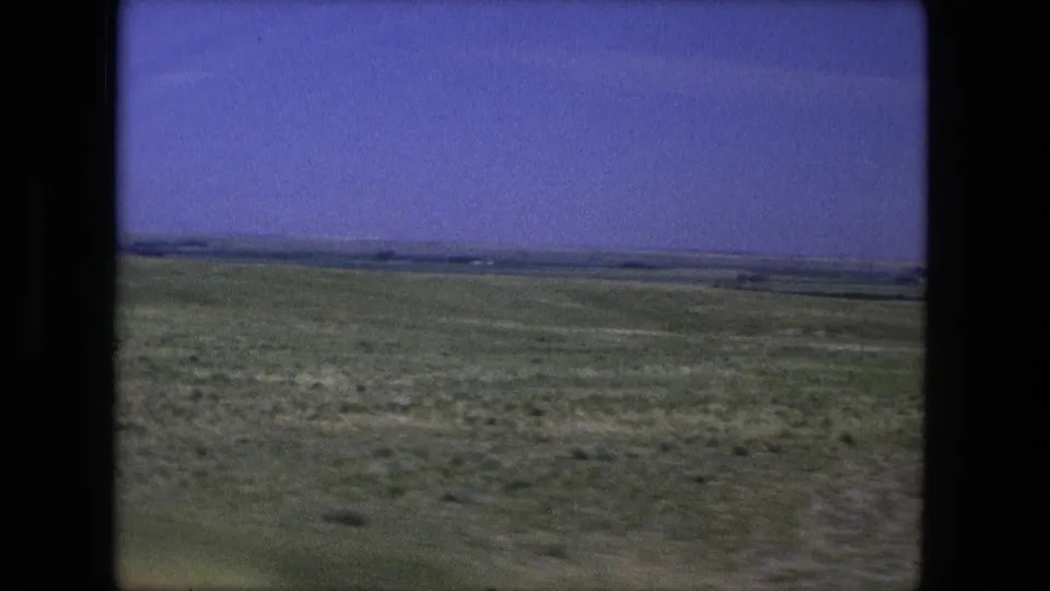 1976 8mm view of broad grassland and distant terrain near Fort Wayne, Indiana, seen from a moving road trip perspective.
