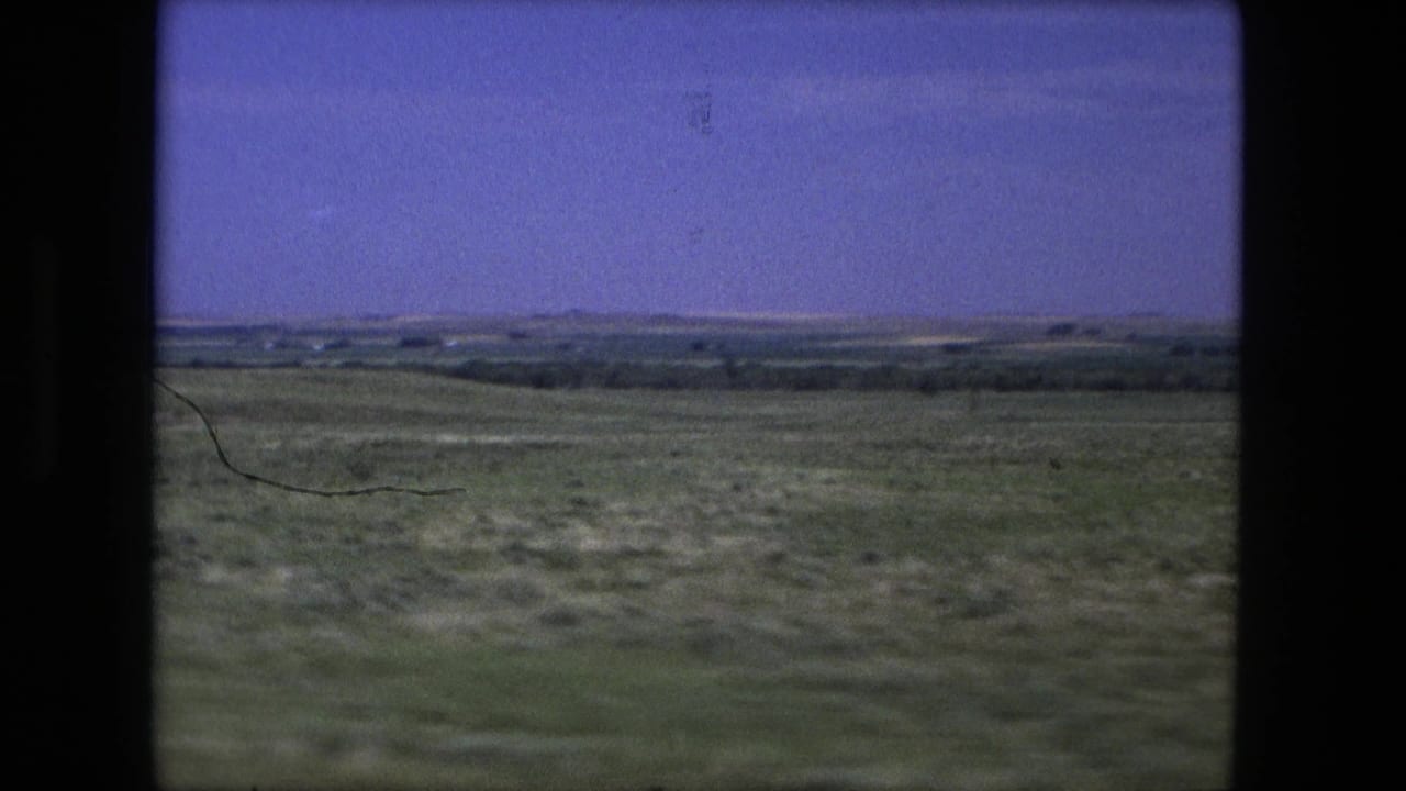 Rolling green terrain with distant tree lines and a hazy horizon under blue sky.