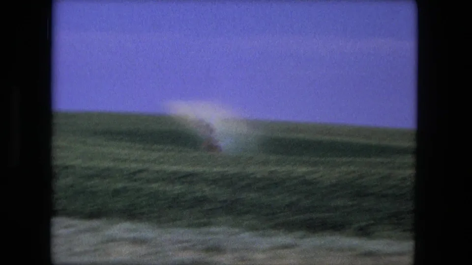 1976 8mm home-movie frame from the Fort Wayne, Indiana metadata showing a moving view over green grass and a soft dust trail.