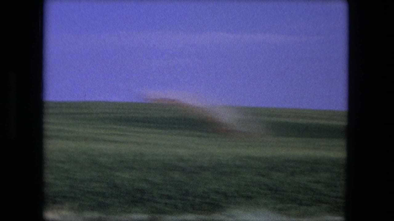1976 8mm frame associated with Fort Wayne, Indiana, showing open grassland, a low horizon, and a blurred dust plume.