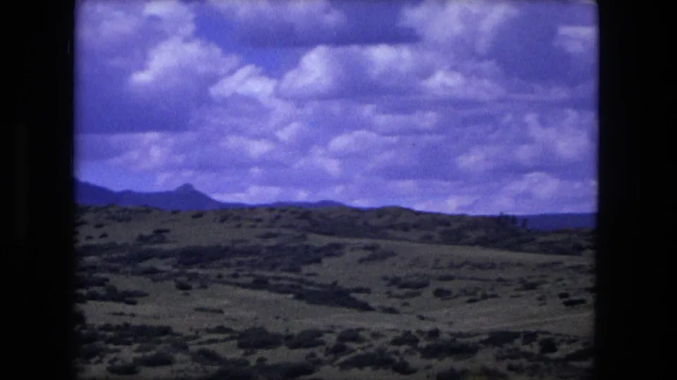 1976 home-movie view of rural landscape near Fort Wayne, Indiana, with low hills, scattered trees, and a cloud-filled sky.