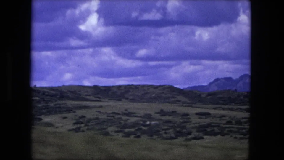 8mm frame of rural Indiana fields and low hills near Fort Wayne, with dramatic clouds and a purple-blue film color cast.
