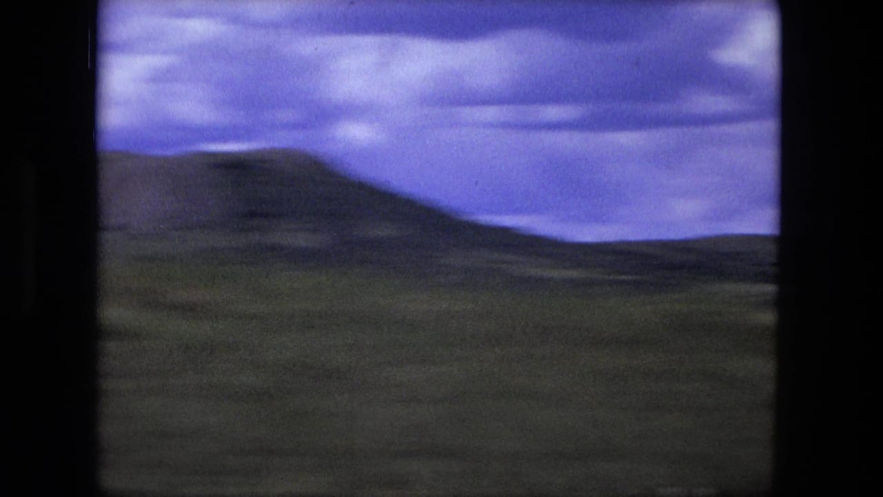 Wide scrubland and low hills under a cloudy purple-blue sky, seen through a film frame.