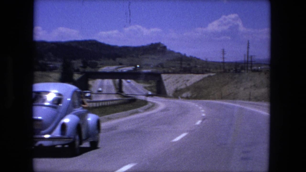 Blue vintage Beetle traveling on a divided highway toward a concrete overpass.