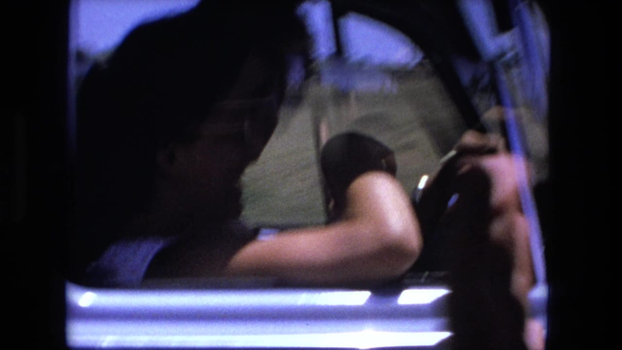 Driver seen through an open car window with one arm near the steering wheel.