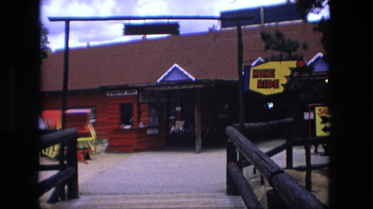Red entrance building with wooden rails, pine trees, and a yellow Mine Ride sign at right.