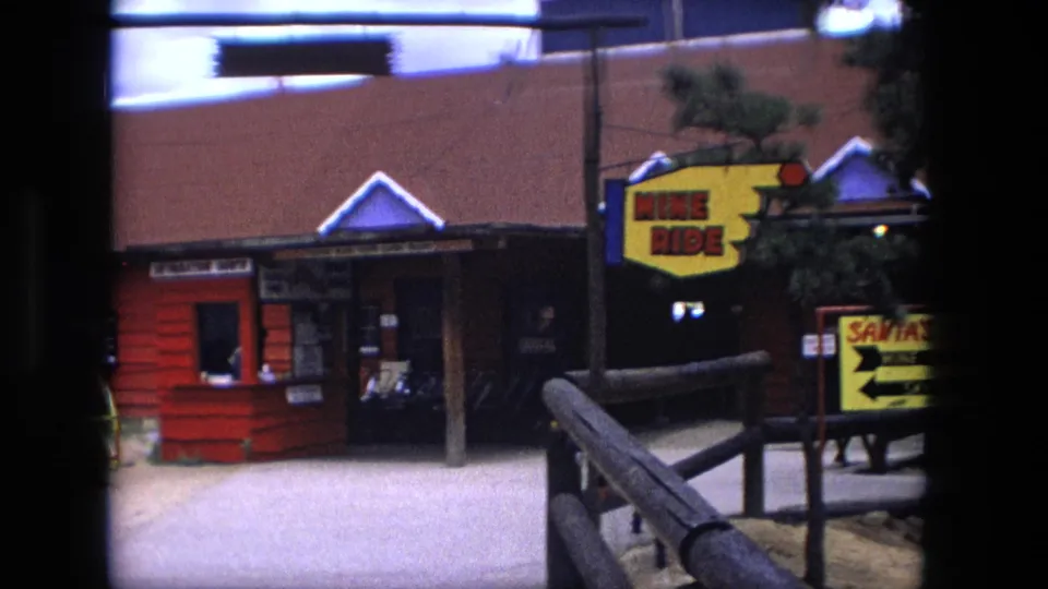 1976 Fort Wayne amusement park view with Mine Ride signage, Santa's Rides direction board, wooden rails, and a red building.