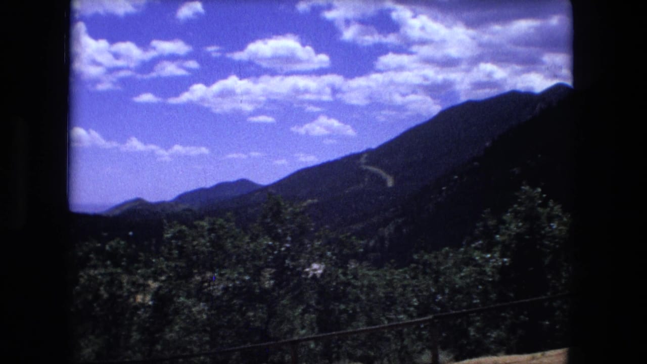 Pine-covered mountains under a bright sky with scattered clouds.