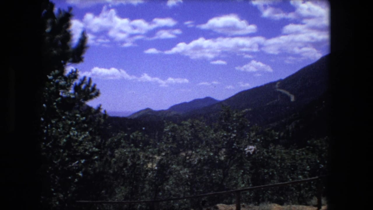 Archival 8mm view of wooded hills and a distant mountain ridge beneath a bright clouded sky.